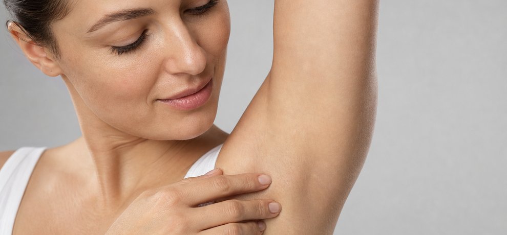 Gros plan sur l'aisselle nette d'une femme en débardeur blanc sur fond gris clair, illustrant une transpiration maîtrisée au naturel