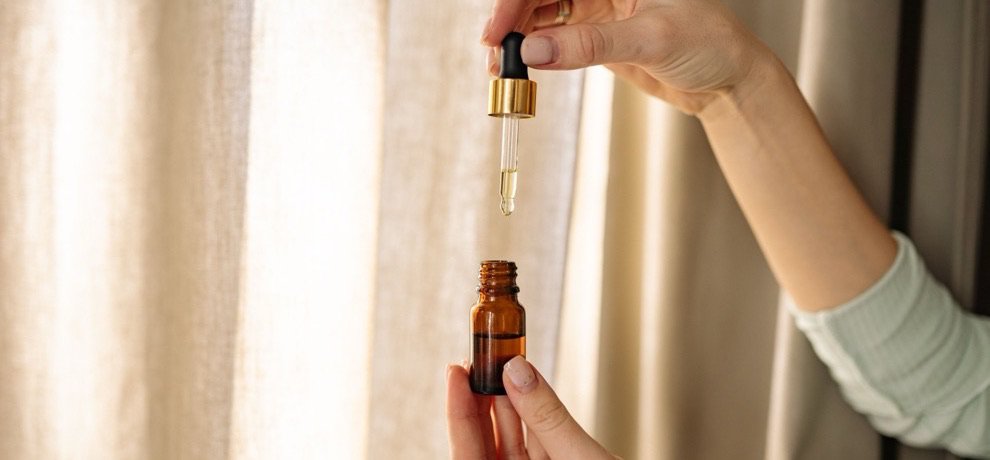 Mains dosant une Huile Essentielle à la pipette au-dessus d'un flacon ambré, goutte à goutte